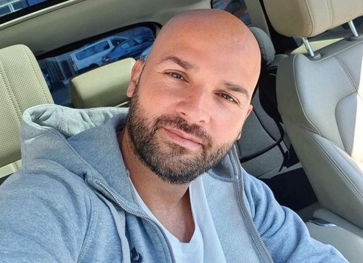 Andrei Ștefănescu într-o bluză gri și tricou alb, stă în mașină și nu are păr