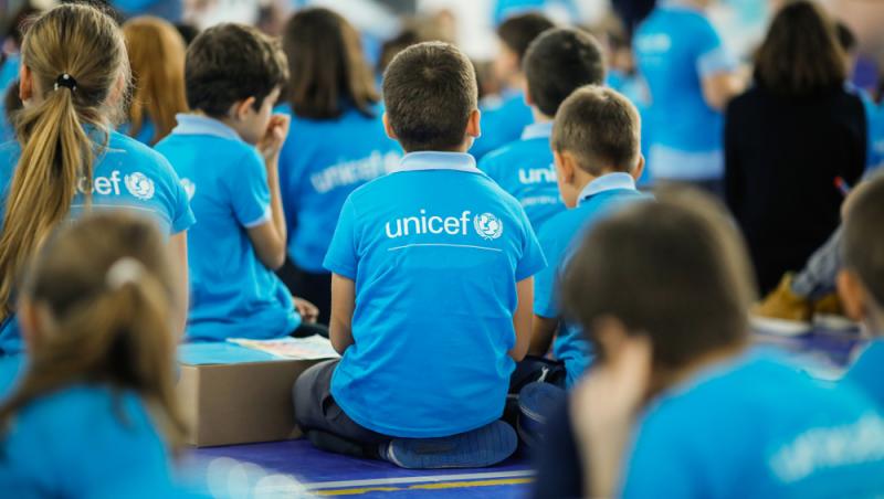 copii în tricouri unicef care stau cu spatele la cameră